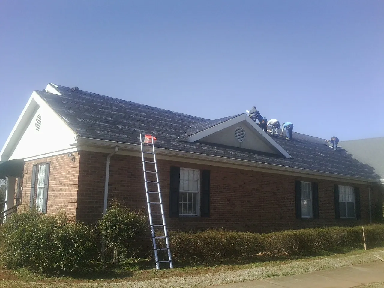Crew tearing shingles off a brick ranch roof with a ladder set — Metal Roof Repair work by our crew in Elizabethton
