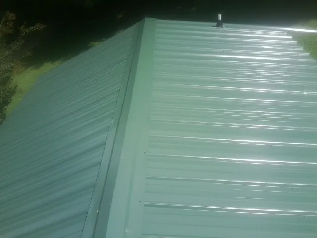 New green metal panels meeting at the ridge of a roof — Flat Roof Repair work by our crew in Elizabethton