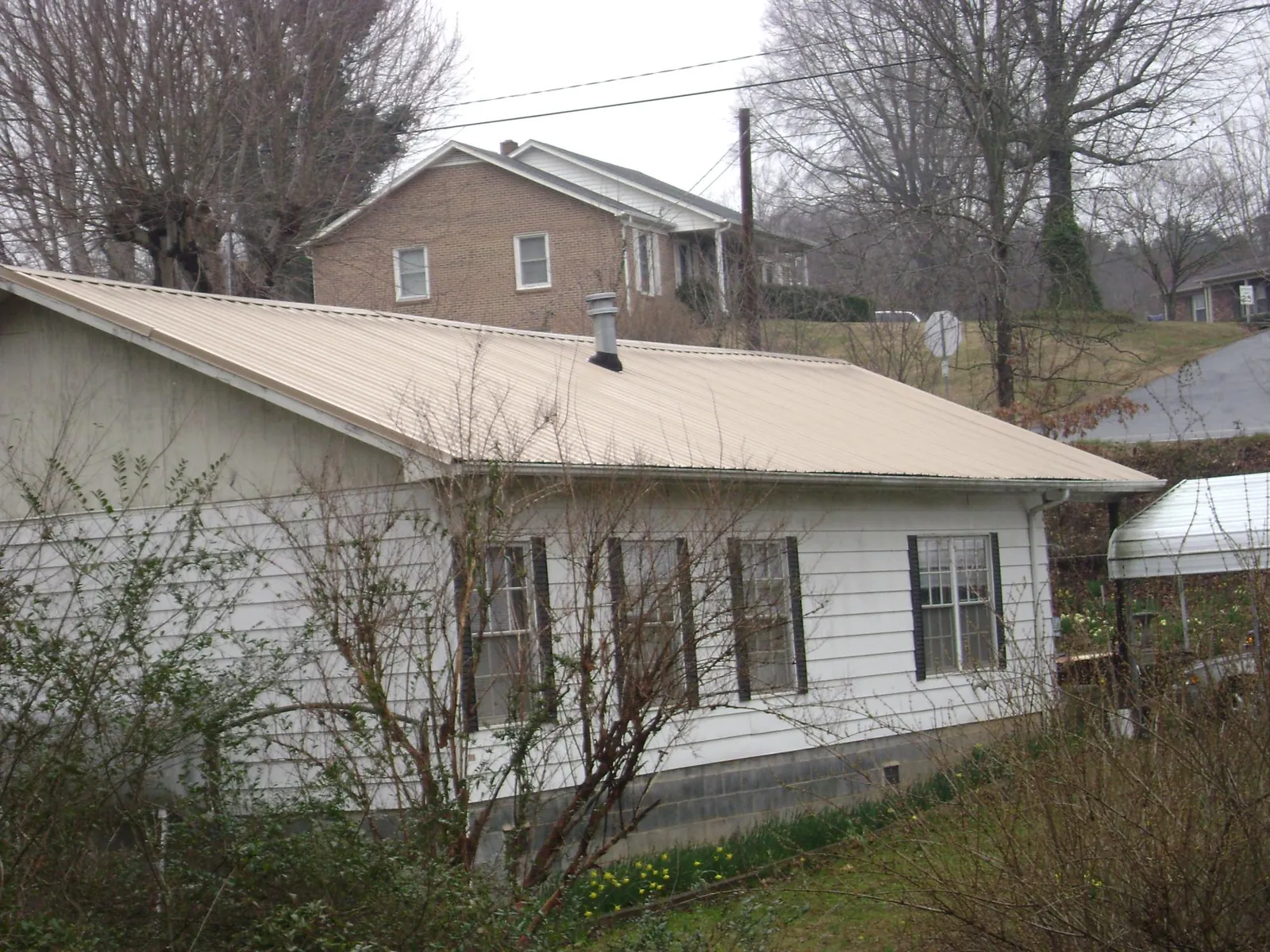 Tan metal roof on a white sided house set into a hillside — Commercial Roofing by Roofing Brothers in Elizabethton